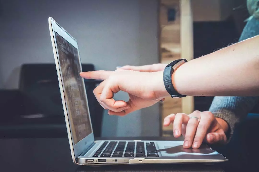 Person pointing at laptop screen during a presentation.