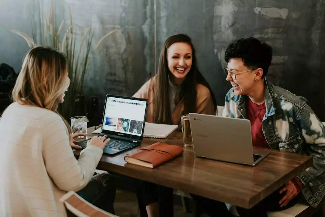 Three people collaborating with laptops at a table.