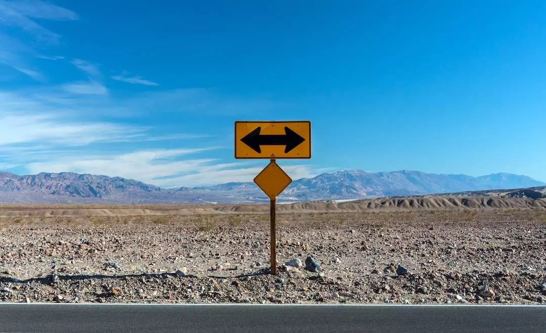 Desert road with two-way arrow sign and mountains.