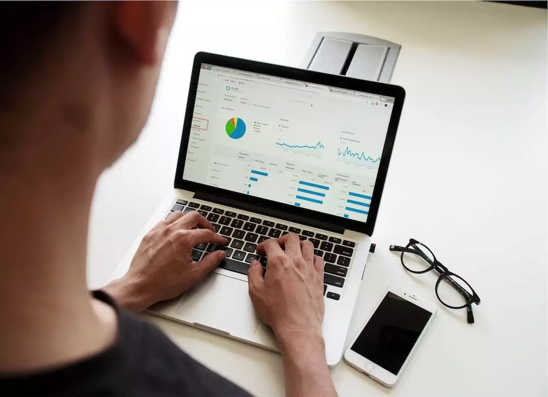 Person analyzing data on laptop with glasses and smartphone.