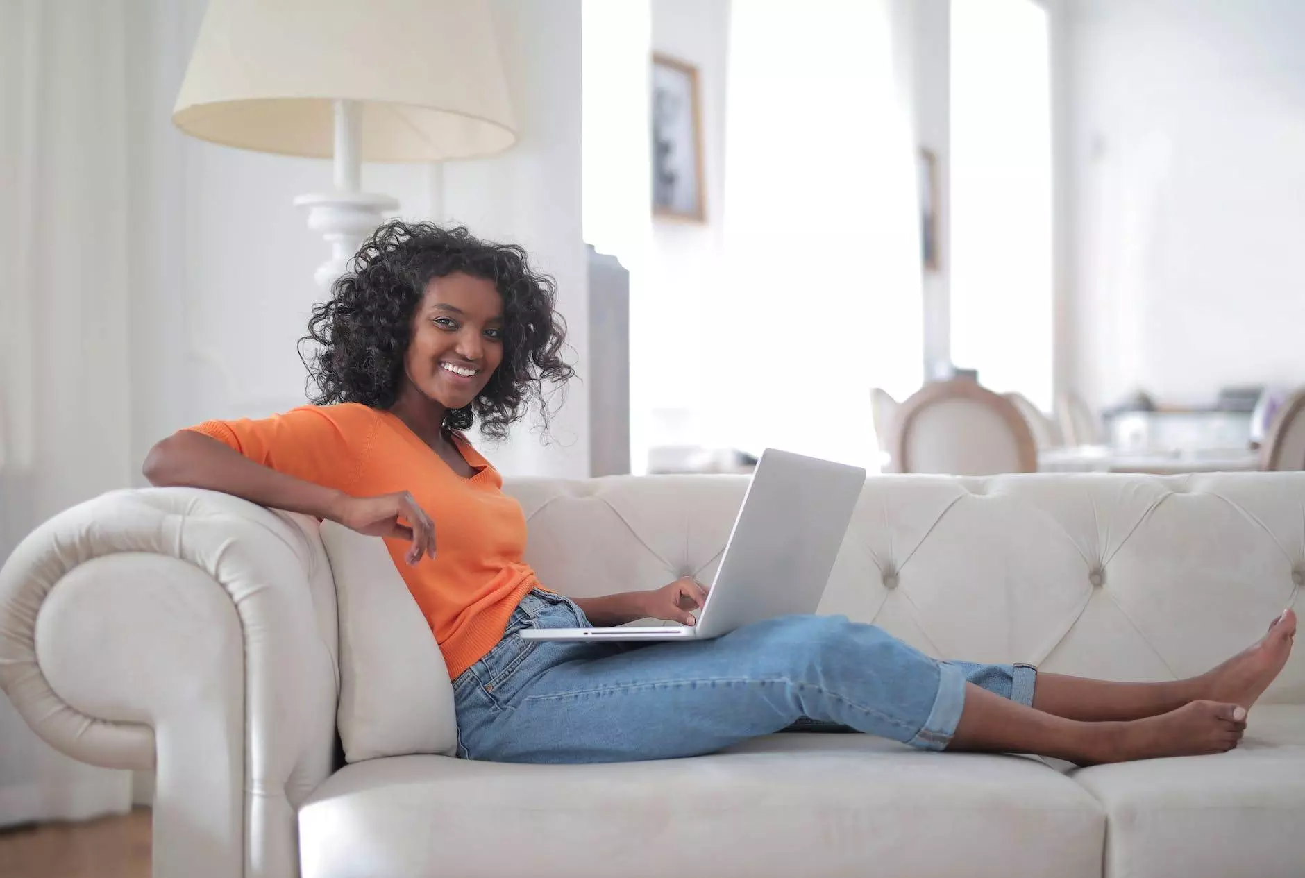 positive young ethnic lady sitting on sofa with laptop and looking at camera