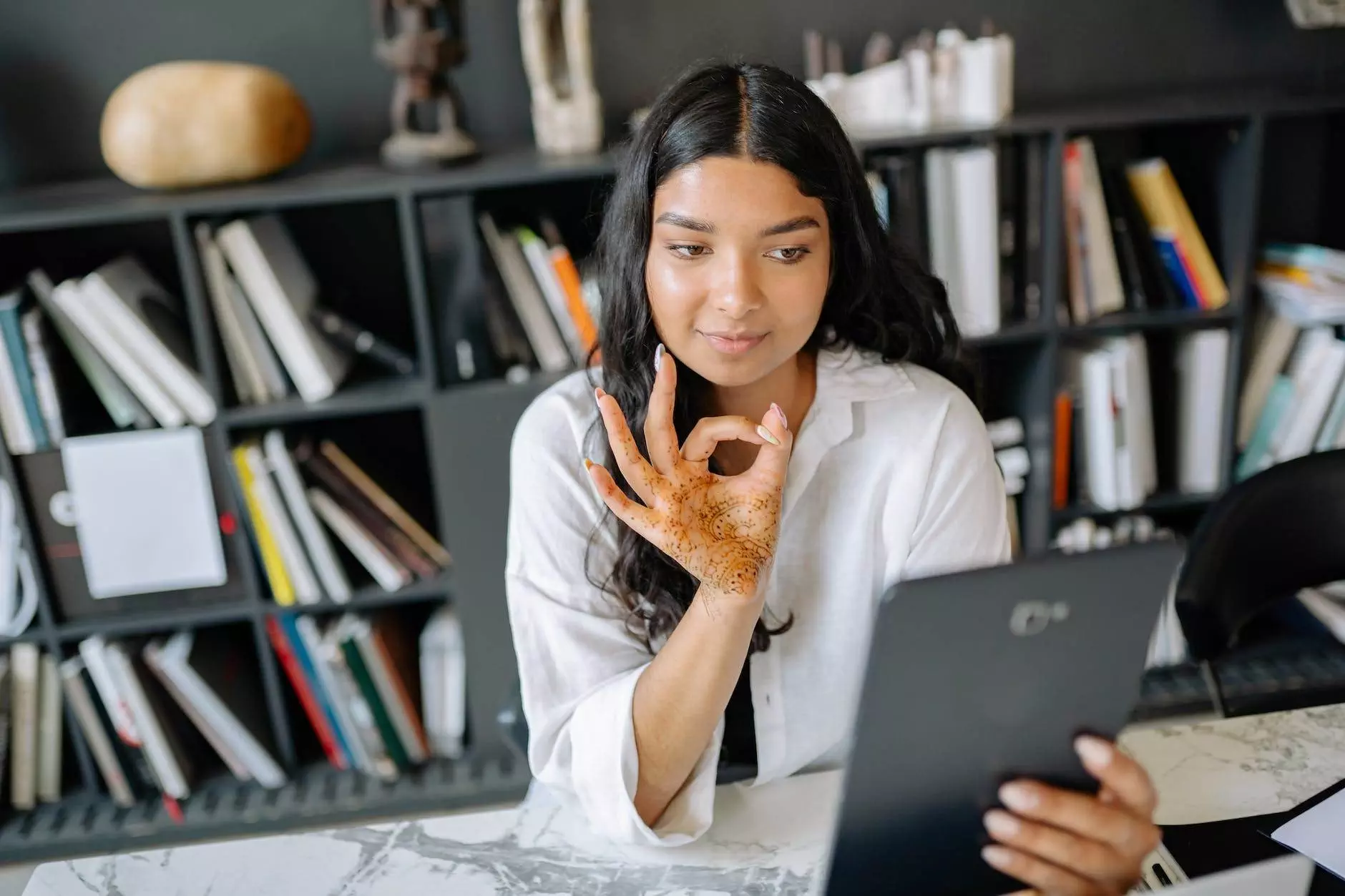 woman sitting at a desk and showing an okay sign on a video call on a tablet