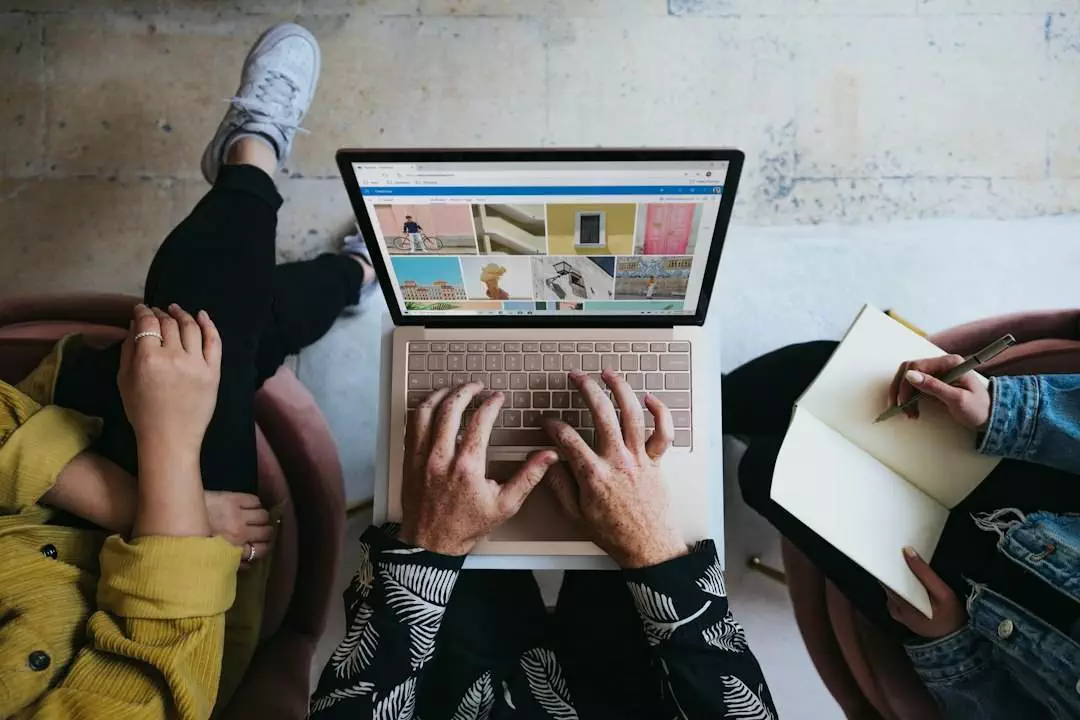 Person using laptop beside individual writing in notebook