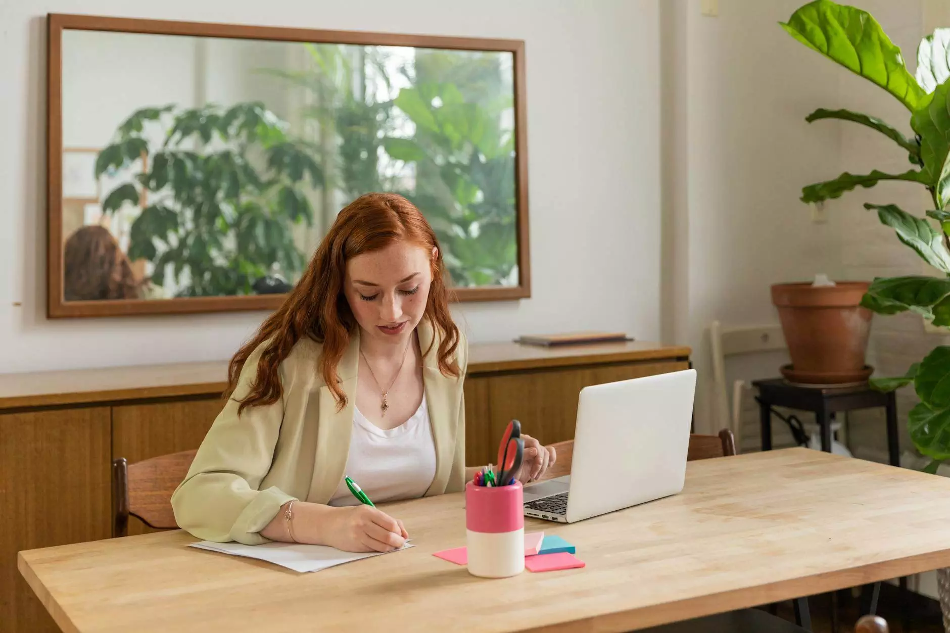 young woman sitting at the desk with a laptop and writing on a piece of paper