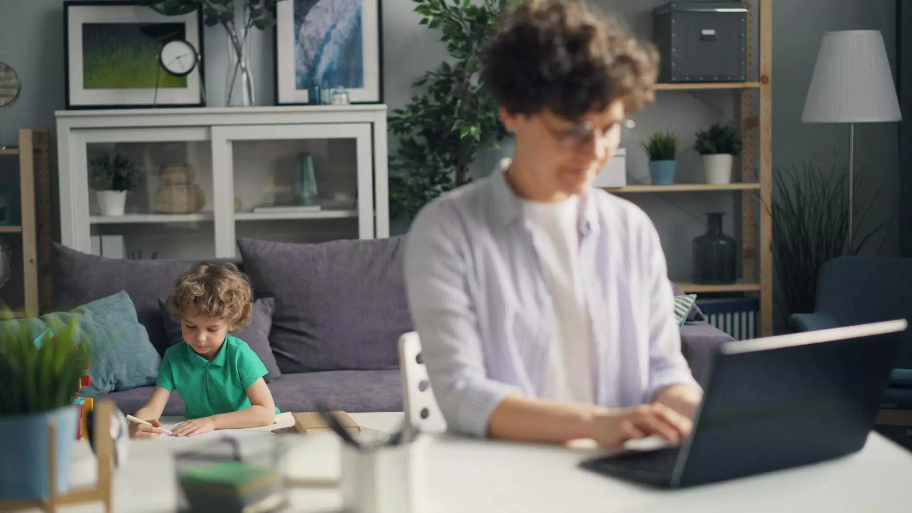 mother working on laptop and son playing behind