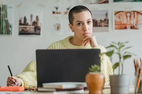 thoughtful woman with stylus at table with laptop